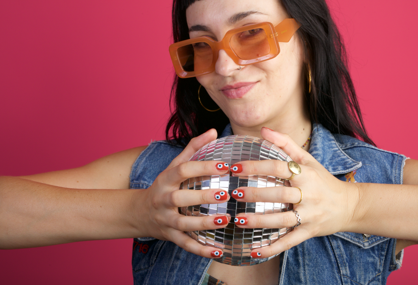 Person holding a disco ball showing her hands with red nail wraps which sown blue eyes