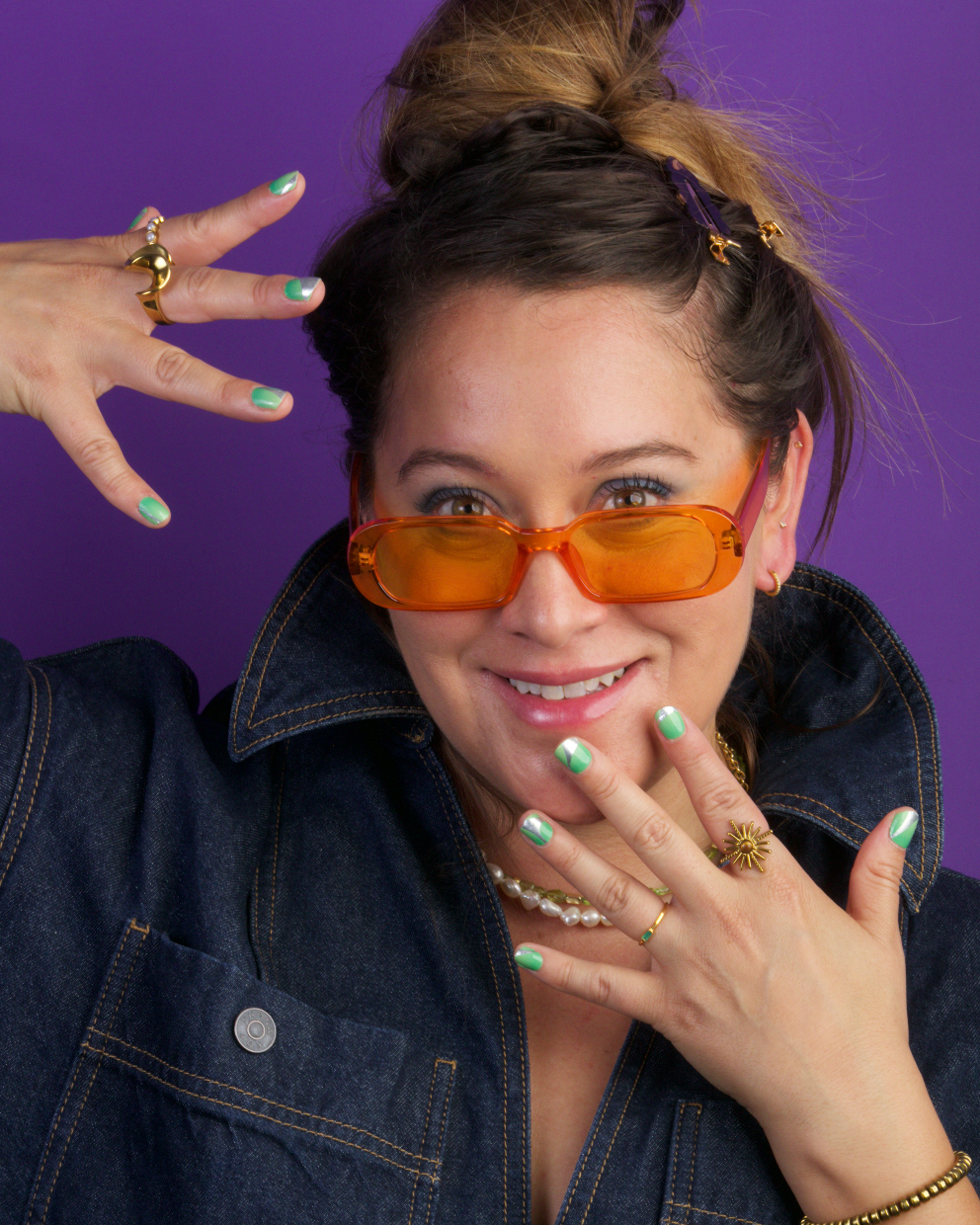 Person wearing orange sunglasses showing her hands with green nail wraps and various rings