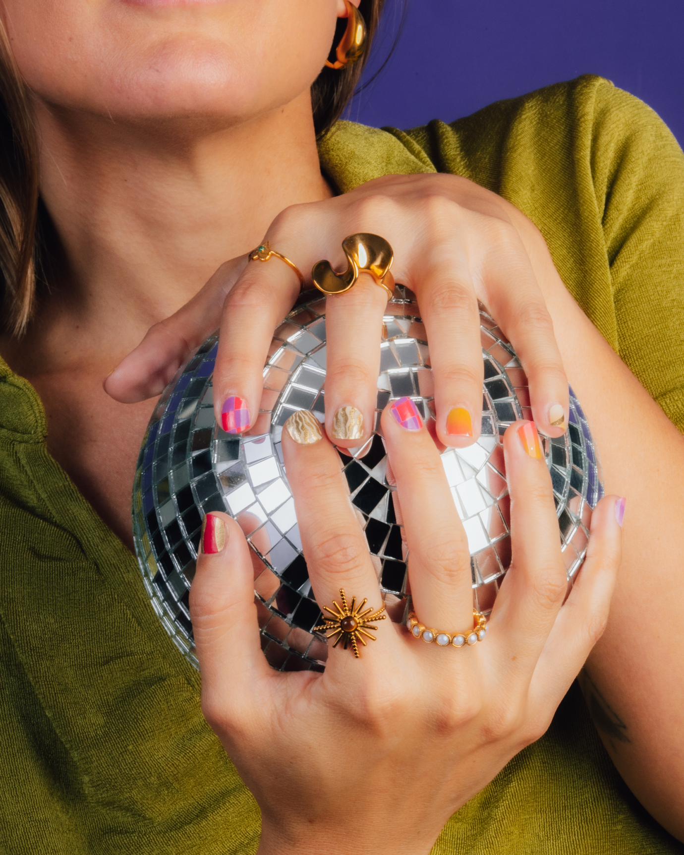 Person holding a disco ball with colorful nails wraps against a purple background